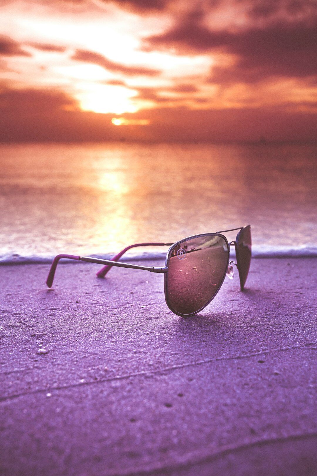 Polarized sunglasses resting on sand near the ocean